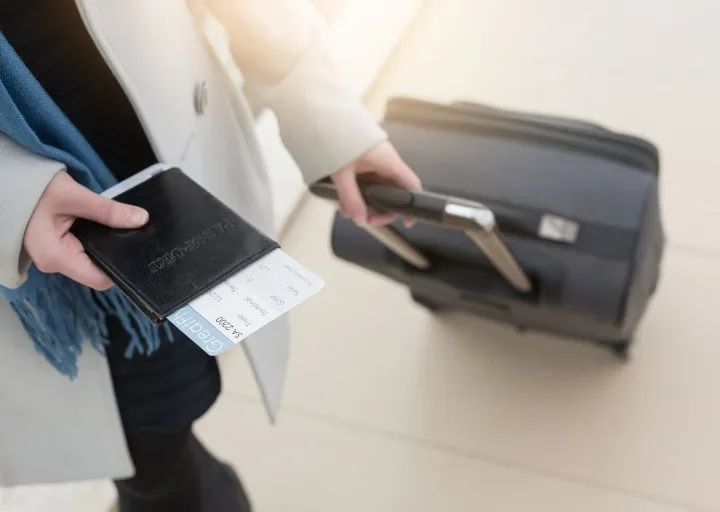 Pessoa com mãos em passaporte e carregando mala de viagem